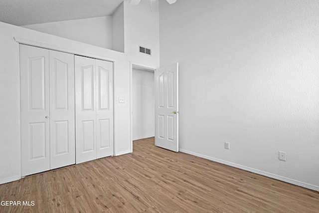 unfurnished bedroom featuring ceiling fan, light wood-type flooring, a textured ceiling, high vaulted ceiling, and a closet