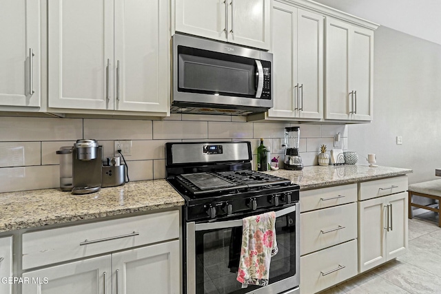 kitchen featuring tasteful backsplash, white cabinetry, appliances with stainless steel finishes, light tile patterned floors, and light stone counters