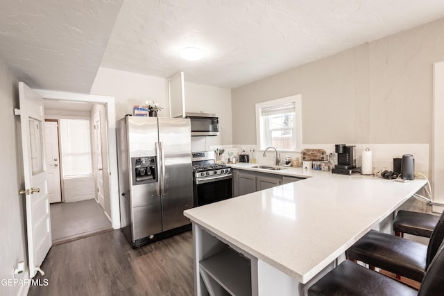 kitchen with appliances with stainless steel finishes, sink, kitchen peninsula, dark wood-type flooring, and gray cabinets