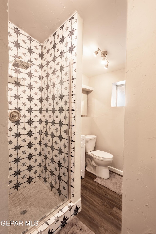 bathroom with hardwood / wood-style floors, toilet, and a tile shower