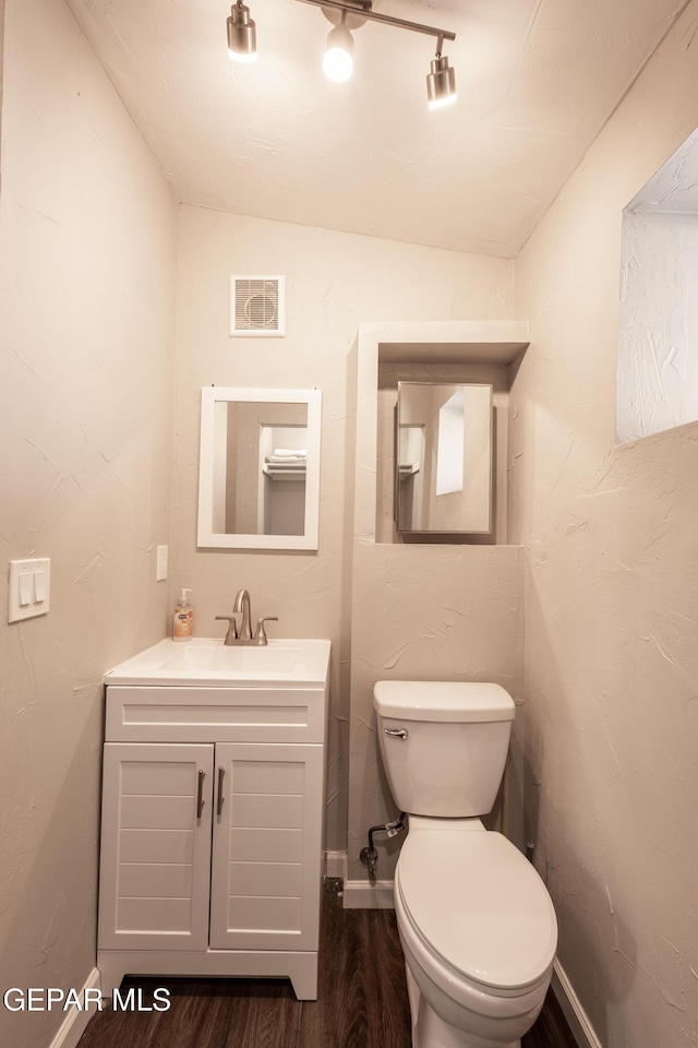 bathroom featuring hardwood / wood-style flooring, track lighting, toilet, vanity, and lofted ceiling