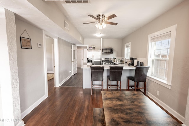 kitchen featuring a kitchen bar, sink, kitchen peninsula, stainless steel appliances, and dark hardwood / wood-style floors