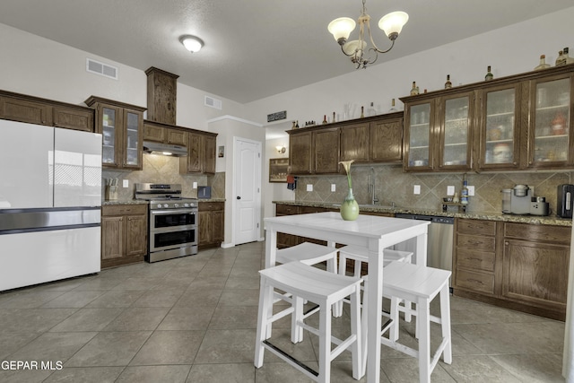 kitchen with sink, light tile patterned floors, pendant lighting, stainless steel appliances, and light stone countertops