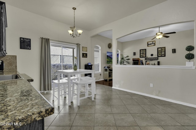 dining space with sink, ceiling fan with notable chandelier, vaulted ceiling, and dark tile patterned floors