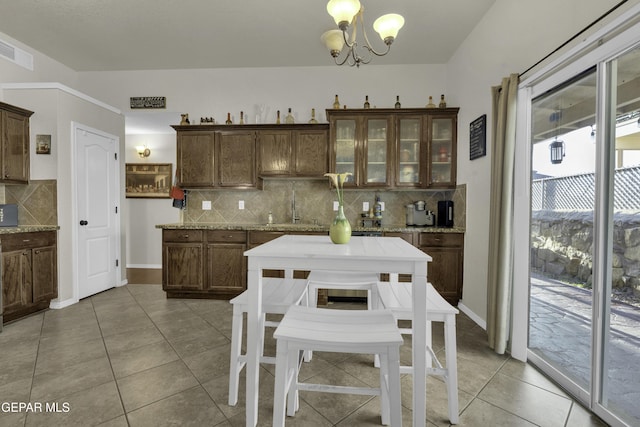 kitchen with light stone counters, hanging light fixtures, light tile patterned floors, and dark brown cabinets