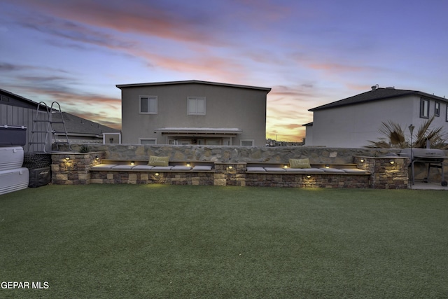 back house at dusk featuring a lawn