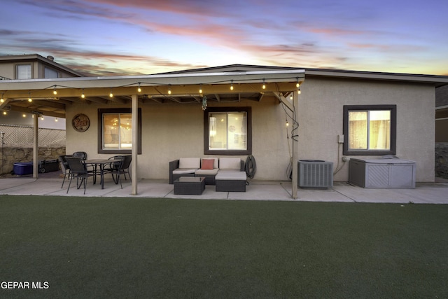 back house at dusk with a yard, central AC unit, and a patio area