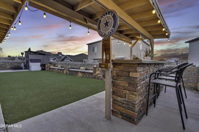 patio terrace at dusk with a yard and an outdoor bar