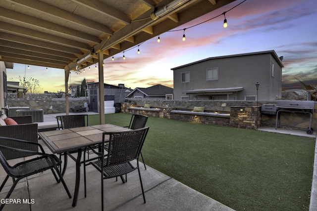 patio terrace at dusk featuring cooling unit, grilling area, a lawn, and exterior kitchen