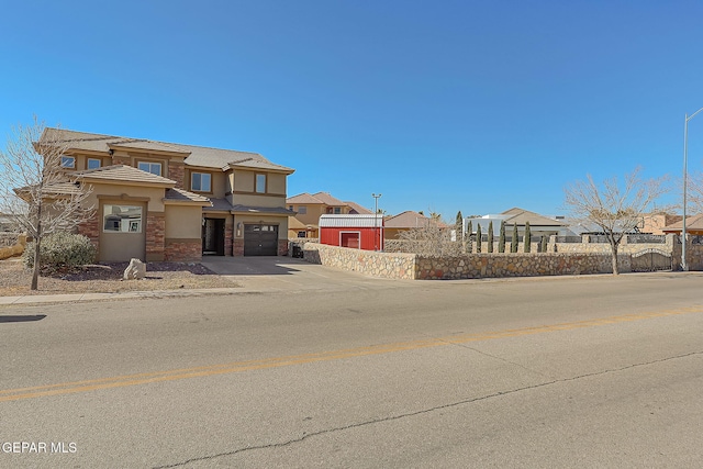 view of front facade with fence, driveway, stucco siding, stone siding, and a garage