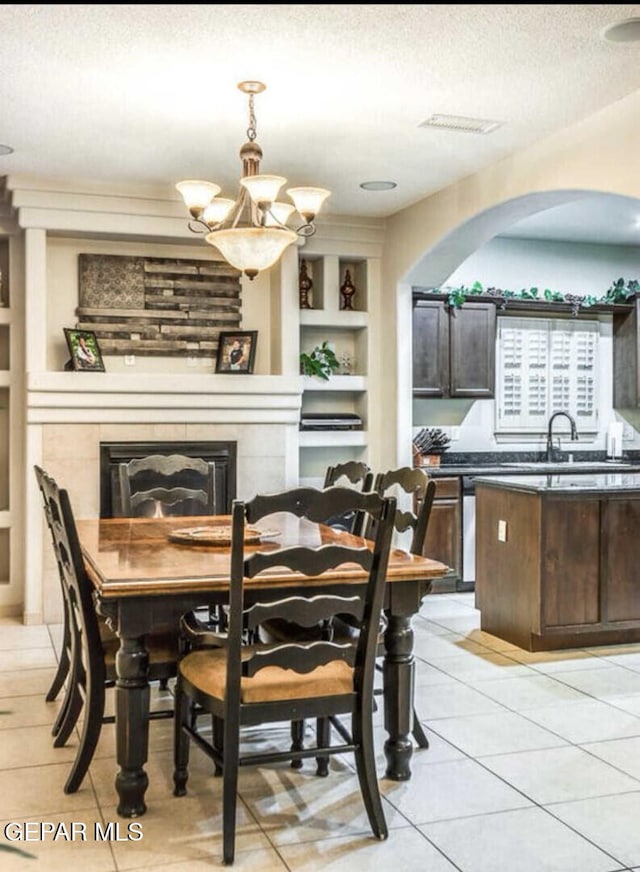 tiled dining room featuring a fireplace, built in features, a textured ceiling, a chandelier, and sink