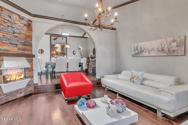 living room featuring wood-type flooring, ornamental molding, a stone fireplace, and an inviting chandelier