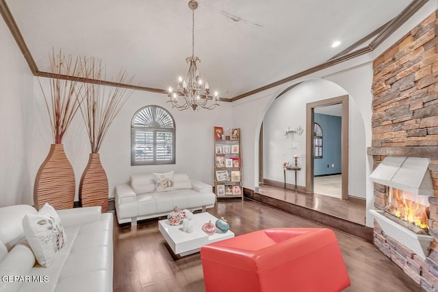 living room featuring dark wood-type flooring, a notable chandelier, ornamental molding, and a stone fireplace