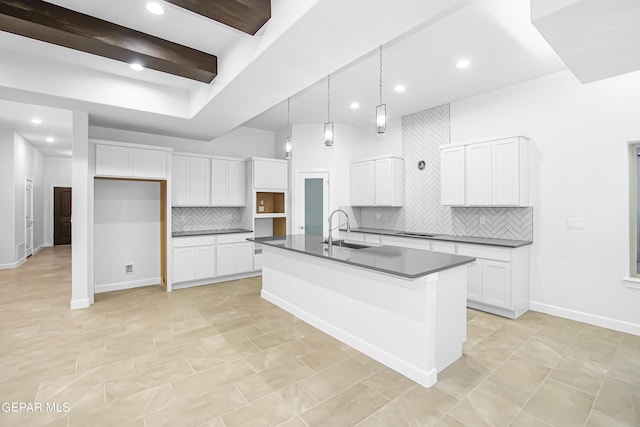 kitchen featuring sink, hanging light fixtures, white cabinets, and a center island with sink