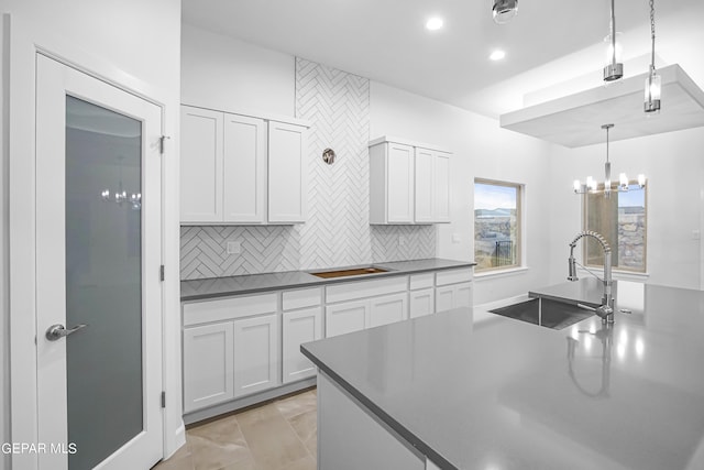 kitchen with hanging light fixtures, sink, white cabinets, and decorative backsplash