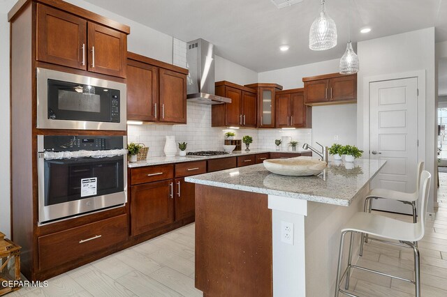 1022 Callie Ct, Socorro, TX 79927 - kitchen with stainless steel appliances, backsplash, glass insert cabinets, wall chimney range hood, and light stone countertops