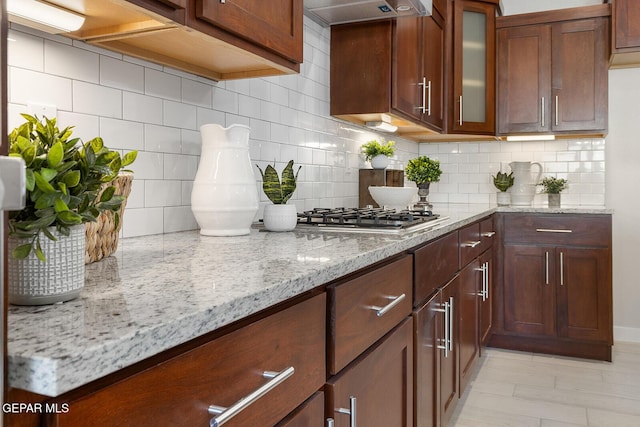 1022 Callie Ct, Socorro, TX 79927 - kitchen featuring tasteful backsplash, glass insert cabinets, light stone countertops, under cabinet range hood, and stainless steel gas stovetop