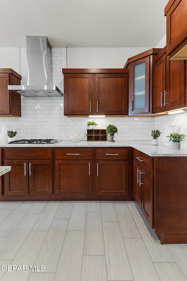 1022 Callie Ct, Socorro, TX 79927 - kitchen featuring wall chimney exhaust hood, glass insert cabinets, light stone counters, stainless steel gas stovetop, and backsplash