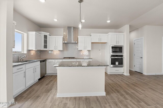 kitchen featuring sink, white cabinetry, a center island, stainless steel appliances, and wall chimney range hood