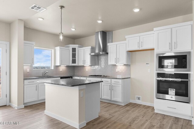 kitchen with pendant lighting, white cabinetry, a center island, stainless steel appliances, and wall chimney range hood