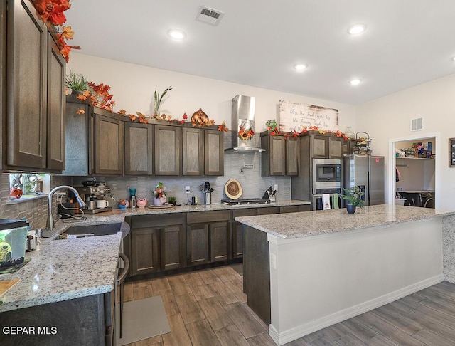 kitchen featuring wall chimney range hood, light stone counters, stainless steel appliances, and a center island