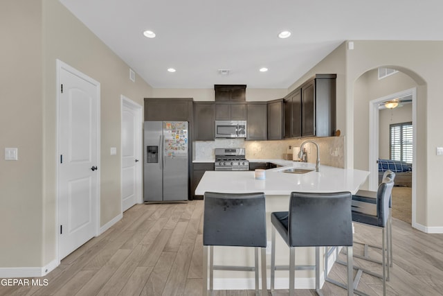 kitchen featuring appliances with stainless steel finishes, sink, dark brown cabinetry, kitchen peninsula, and light wood-type flooring