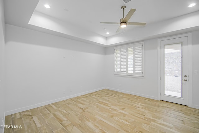 empty room with light hardwood / wood-style flooring, a raised ceiling, and ceiling fan