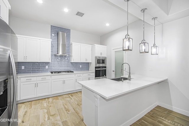 kitchen with sink, stainless steel appliances, white cabinets, kitchen peninsula, and wall chimney exhaust hood