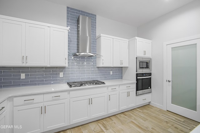 kitchen with white cabinetry, wall chimney range hood, decorative backsplash, and stainless steel appliances