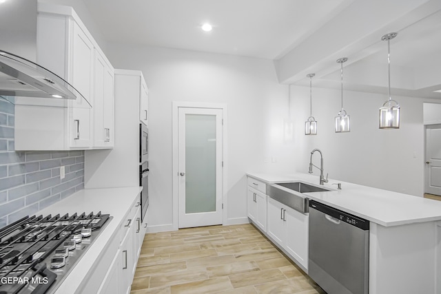 kitchen with sink, appliances with stainless steel finishes, white cabinetry, decorative backsplash, and wall chimney exhaust hood