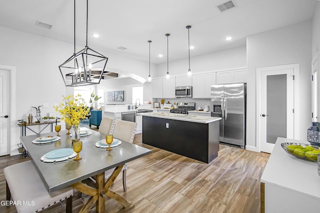 kitchen with pendant lighting, appliances with stainless steel finishes, white cabinetry, tasteful backsplash, and a kitchen island