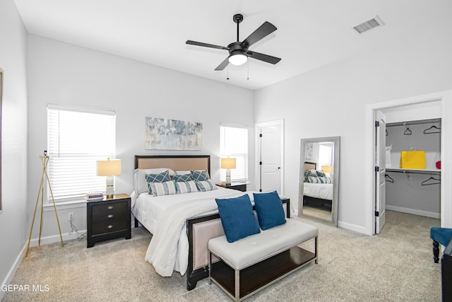 bedroom with ceiling fan, multiple windows, light carpet, and a walk in closet