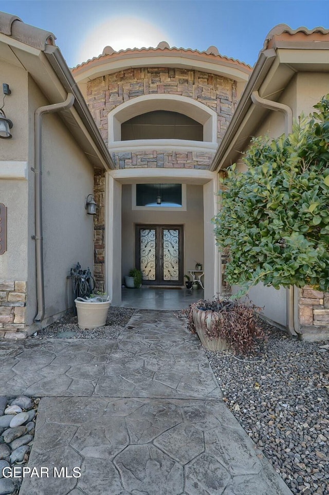 property entrance with stone siding, french doors, and stucco siding