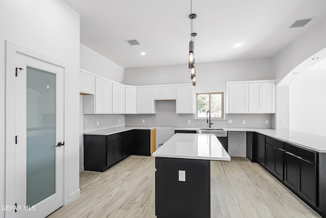 kitchen featuring sink, white cabinetry, a kitchen island, decorative light fixtures, and light wood-type flooring