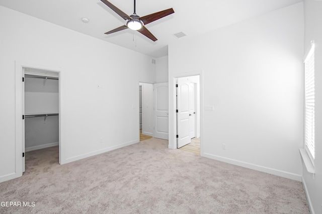 unfurnished bedroom with a spacious closet, light colored carpet, a closet, and ceiling fan