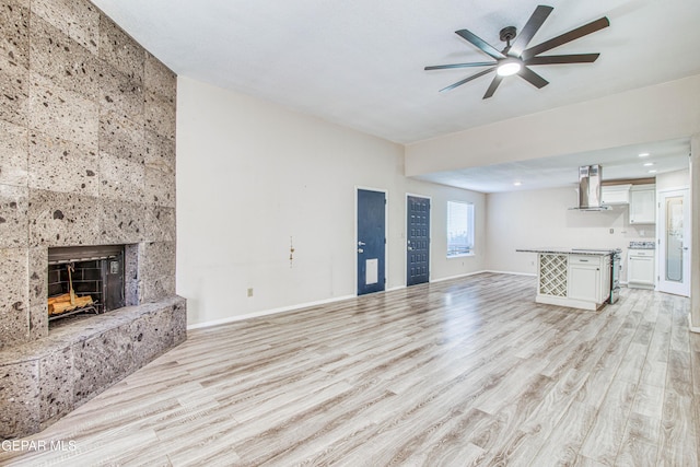 unfurnished living room featuring ceiling fan, a tile fireplace, and light hardwood / wood-style flooring