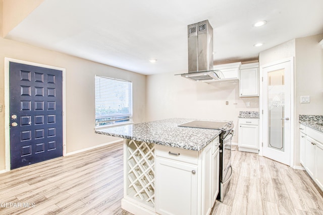 kitchen with electric stove, island range hood, light stone counters, and white cabinetry