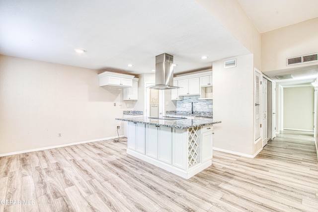 kitchen featuring light hardwood / wood-style floors, a center island with sink, island exhaust hood, dark stone countertops, and white cabinets