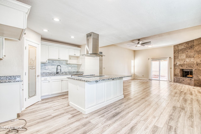 kitchen featuring a fireplace, a kitchen island, white cabinetry, island range hood, and light stone counters