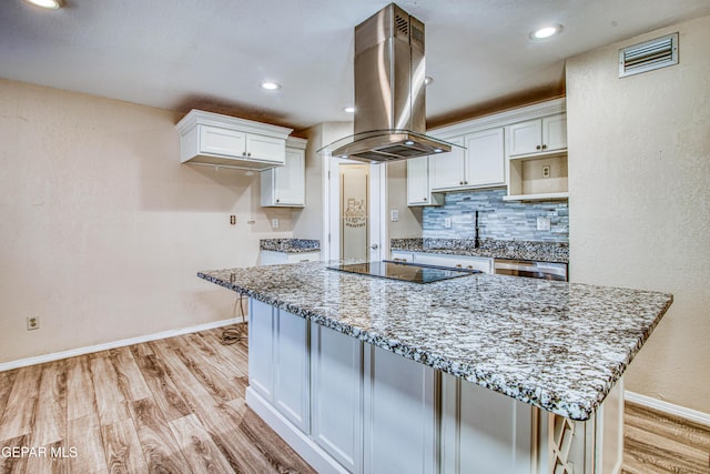 kitchen with light stone counters, island exhaust hood, black electric stovetop, and white cabinetry