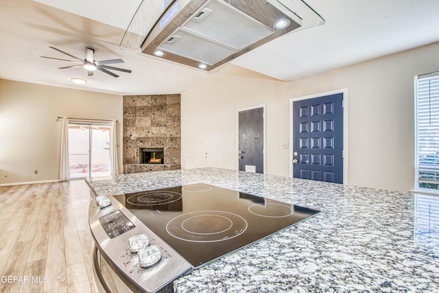 kitchen featuring light hardwood / wood-style floors, ceiling fan, a fireplace, light stone countertops, and cooktop