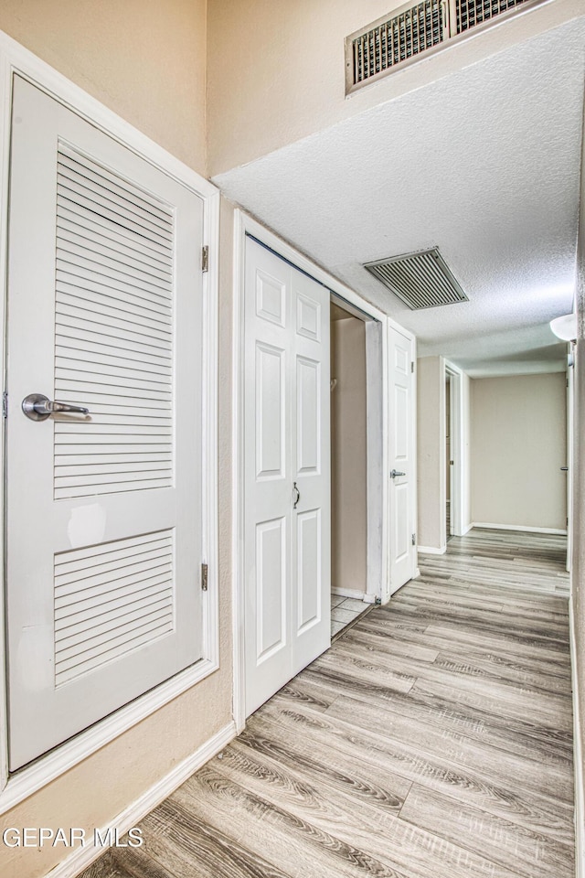 hallway with a textured ceiling and light wood-type flooring