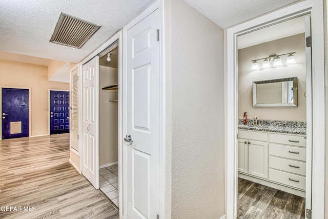 hallway with light wood-type flooring, sink, and a textured ceiling