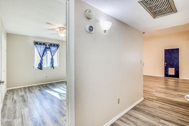 corridor with a textured ceiling and light hardwood / wood-style flooring