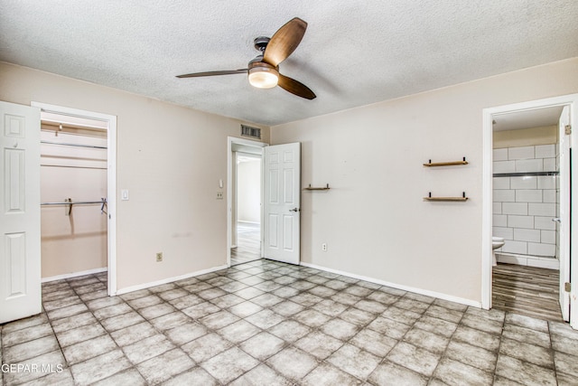 unfurnished bedroom featuring a textured ceiling, ensuite bath, a walk in closet, a closet, and ceiling fan