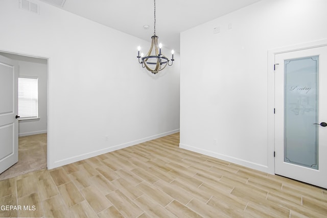 spare room featuring a chandelier and light wood-type flooring