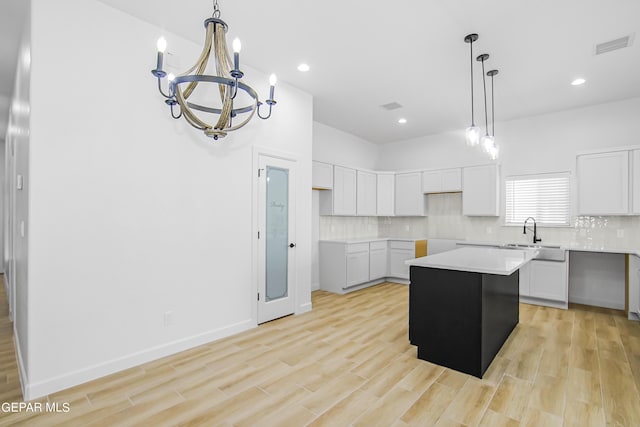 kitchen with decorative light fixtures, tasteful backsplash, sink, white cabinets, and a center island