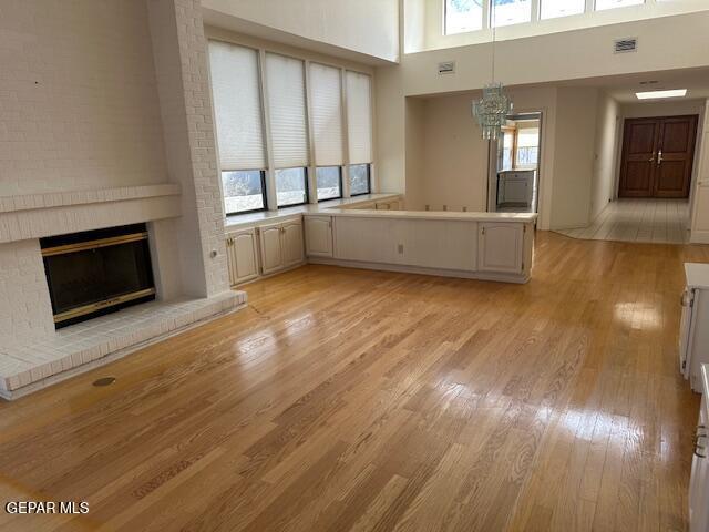 unfurnished living room featuring a high ceiling, a healthy amount of sunlight, light hardwood / wood-style flooring, and a fireplace