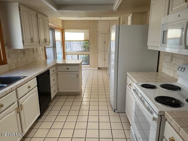 kitchen with kitchen peninsula, white appliances, tile countertops, and a raised ceiling