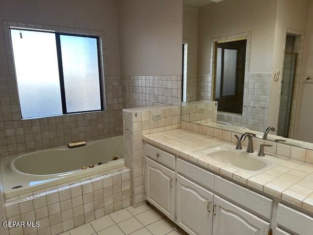 bathroom with a healthy amount of sunlight, tile patterned floors, a relaxing tiled tub, and vanity